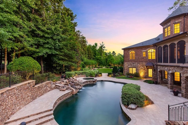 pool at dusk featuring a patio area and an in ground hot tub