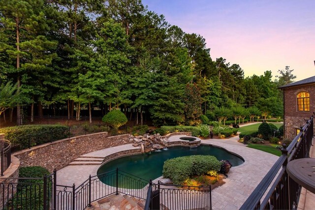 pool at dusk with a patio area and an in ground hot tub