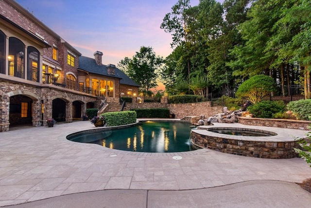 pool at dusk featuring a patio area and an in ground hot tub