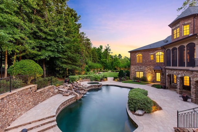 pool at dusk featuring a patio area and an in ground hot tub