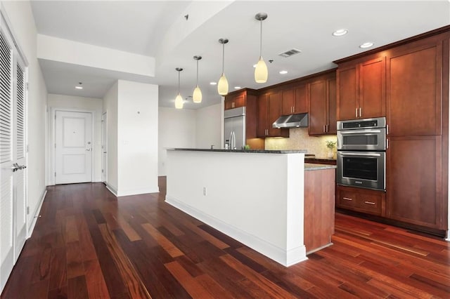 kitchen with dark hardwood / wood-style flooring, tasteful backsplash, stainless steel appliances, a kitchen island with sink, and pendant lighting