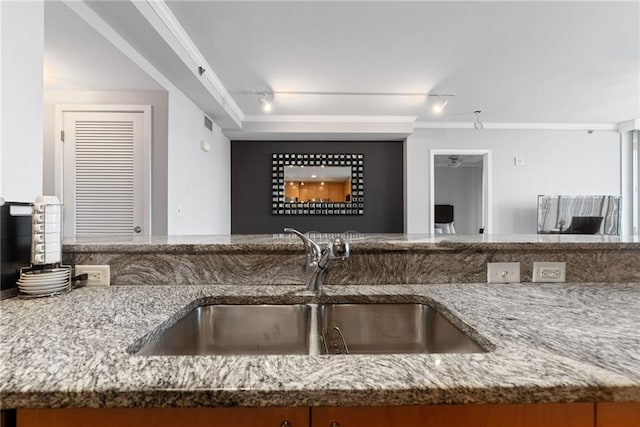 kitchen with crown molding, a sink, rail lighting, and light stone countertops