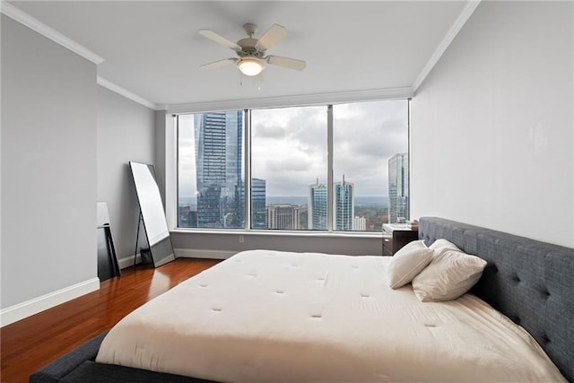 bedroom with ceiling fan, baseboards, wood finished floors, ornamental molding, and a city view