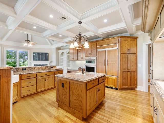 kitchen featuring light wood finished floors, a center island with sink, visible vents, and paneled built in refrigerator