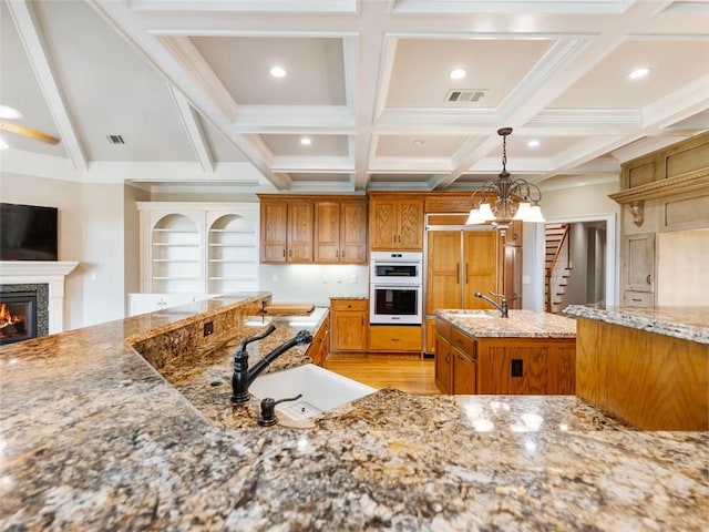 kitchen featuring a sink, white double oven, a glass covered fireplace, and brown cabinets