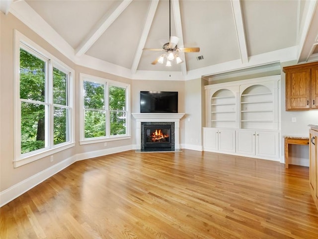 unfurnished living room with beamed ceiling, a glass covered fireplace, and a wealth of natural light