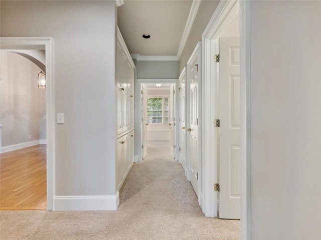 corridor featuring crown molding, baseboards, arched walkways, and light carpet