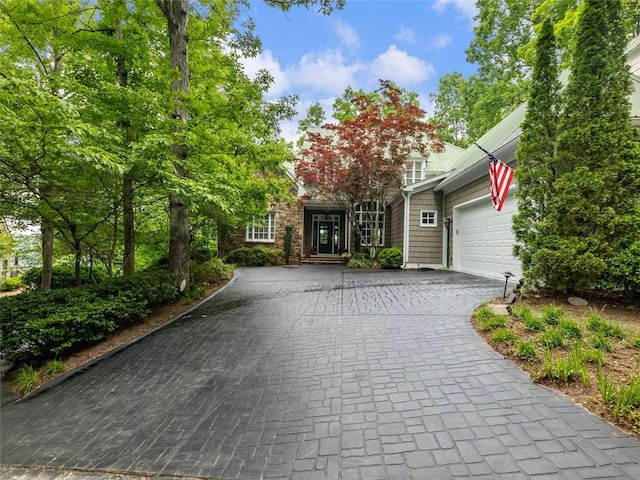 view of property hidden behind natural elements featuring a garage and decorative driveway