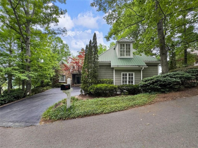 view of property hidden behind natural elements with metal roof and driveway