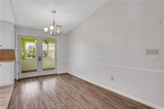 unfurnished dining area featuring visible vents, baseboards, a chandelier, light wood-type flooring, and vaulted ceiling