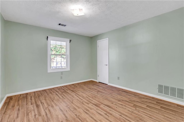 empty room with visible vents, baseboards, a textured ceiling, and wood finished floors