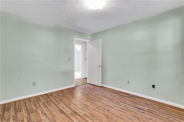 unfurnished room with a textured ceiling, light wood-type flooring, and baseboards