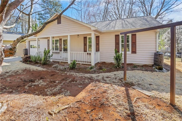 ranch-style house with covered porch, cooling unit, a shingled roof, and a garage