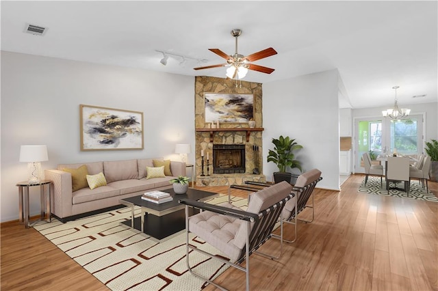 living room with track lighting, visible vents, light wood-type flooring, a stone fireplace, and ceiling fan with notable chandelier