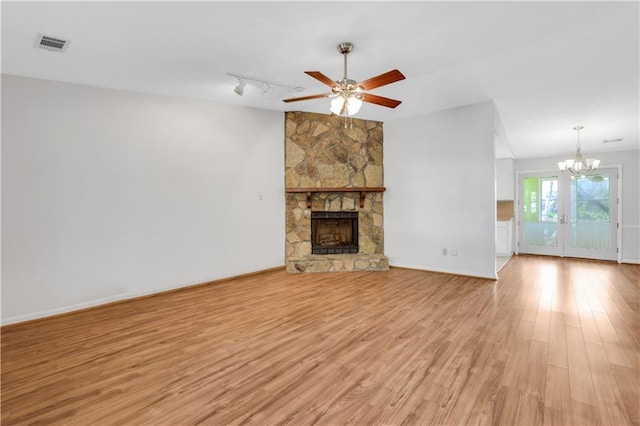 unfurnished living room featuring visible vents, ceiling fan with notable chandelier, light wood-style floors, a stone fireplace, and baseboards