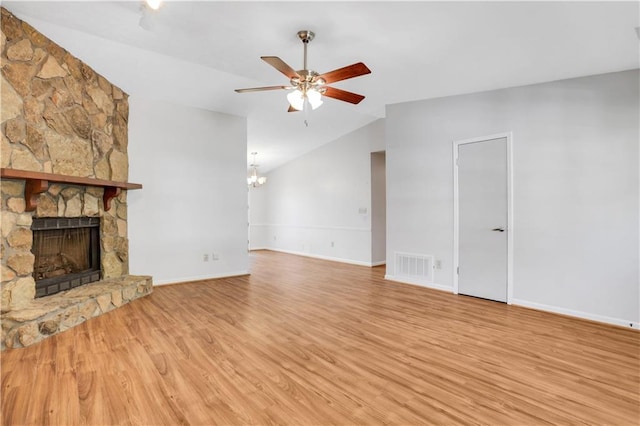 unfurnished living room with visible vents, light wood-type flooring, vaulted ceiling, a stone fireplace, and ceiling fan with notable chandelier