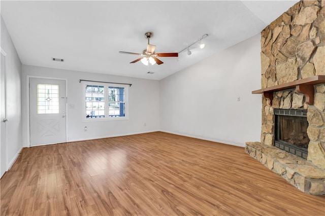 unfurnished living room featuring light wood finished floors, visible vents, baseboards, a stone fireplace, and a ceiling fan