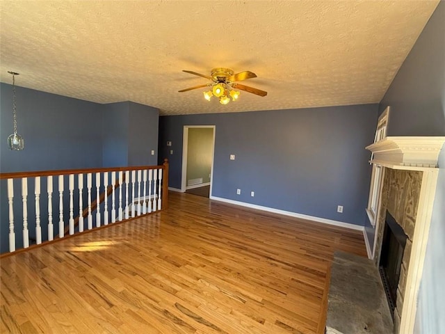 unfurnished living room with a fireplace with flush hearth, a ceiling fan, a textured ceiling, wood finished floors, and baseboards