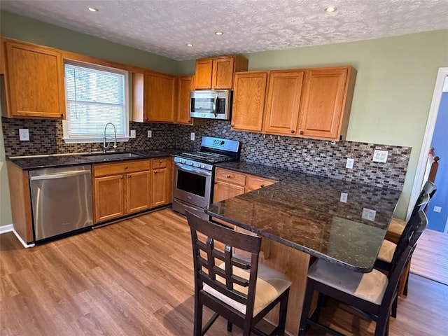 kitchen featuring a breakfast bar area, a peninsula, a sink, appliances with stainless steel finishes, and light wood finished floors