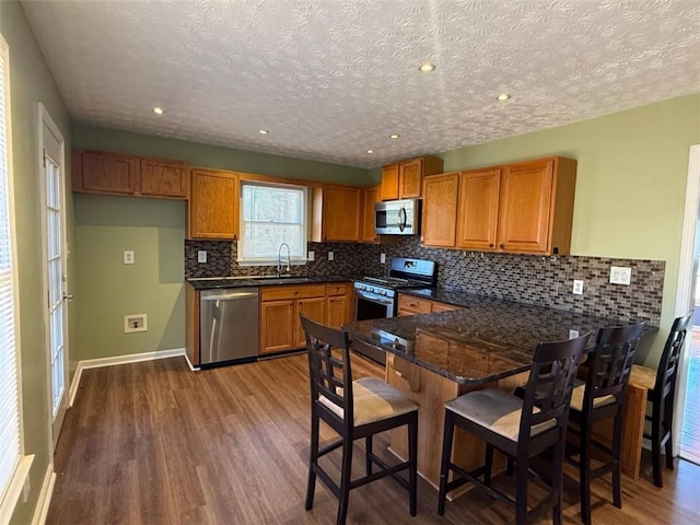 kitchen featuring a peninsula, dark wood-type flooring, a sink, appliances with stainless steel finishes, and brown cabinetry