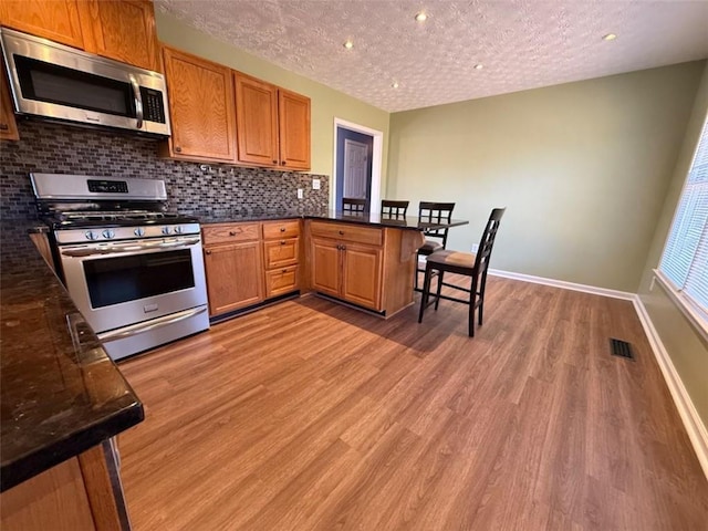 kitchen with light wood finished floors, visible vents, decorative backsplash, a peninsula, and stainless steel appliances