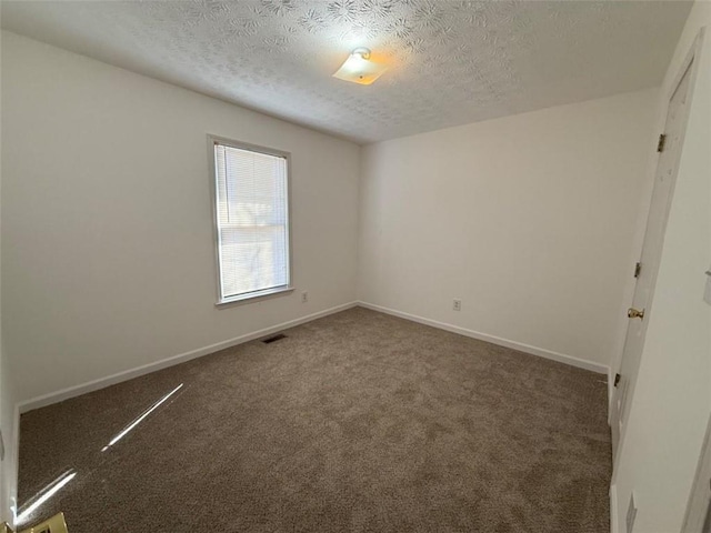 carpeted spare room with a textured ceiling, visible vents, and baseboards