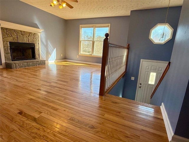 unfurnished living room featuring a textured ceiling, ceiling fan, a fireplace, and wood finished floors