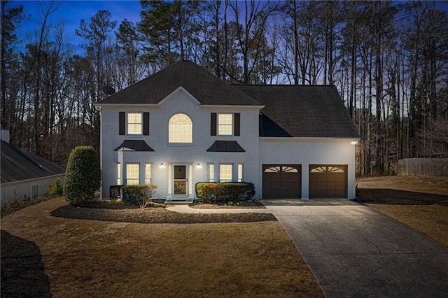 colonial-style house with driveway, brick siding, an attached garage, and a shingled roof