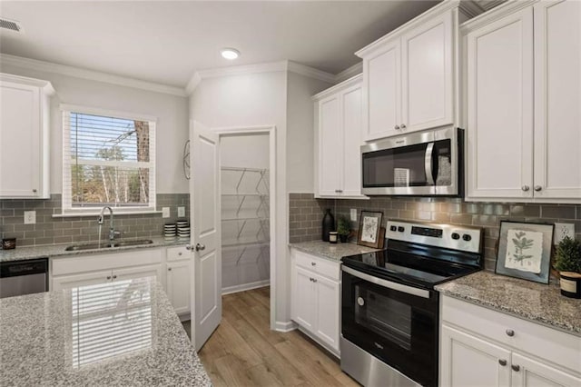 kitchen with sink, white cabinetry, crown molding, appliances with stainless steel finishes, and light stone countertops