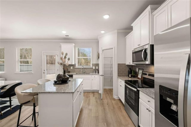 kitchen featuring a breakfast bar area, light stone counters, a kitchen island, stainless steel appliances, and white cabinets