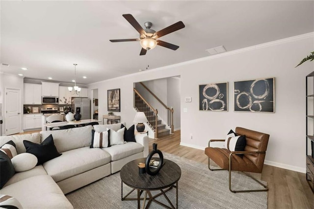 living room with ornamental molding, ceiling fan with notable chandelier, and light wood-type flooring