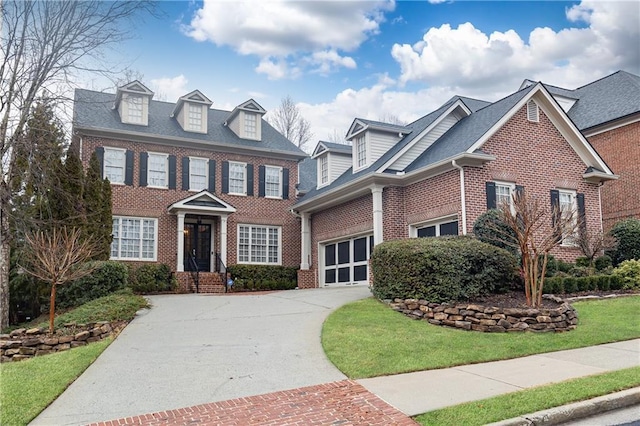 colonial inspired home featuring a garage, concrete driveway, brick siding, and a front lawn