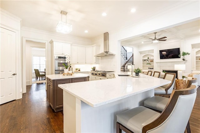 kitchen featuring a center island with sink, wall chimney exhaust hood, a breakfast bar area, open floor plan, and decorative light fixtures