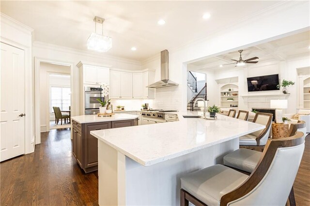 kitchen with a sink, open floor plan, appliances with stainless steel finishes, light stone countertops, and wall chimney exhaust hood