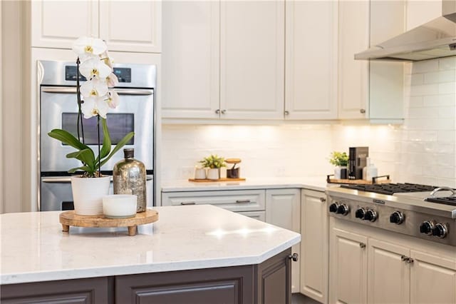 kitchen with stainless steel appliances, white cabinets, wall chimney range hood, and tasteful backsplash