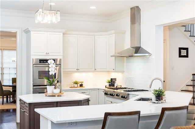 kitchen featuring a center island with sink, light countertops, white cabinets, a sink, and wall chimney range hood