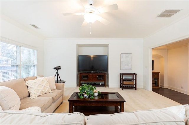 living room featuring arched walkways, crown molding, visible vents, a ceiling fan, and baseboards