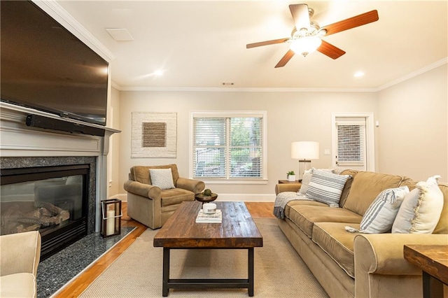 living area featuring ceiling fan, a premium fireplace, baseboards, ornamental molding, and light wood-type flooring