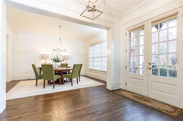 dining room featuring ornamental molding, dark wood-style flooring, an inviting chandelier, french doors, and a decorative wall