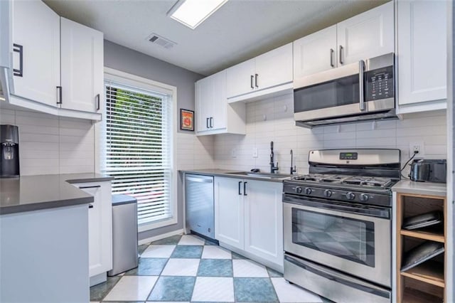 kitchen featuring dark countertops, visible vents, light floors, appliances with stainless steel finishes, and white cabinets