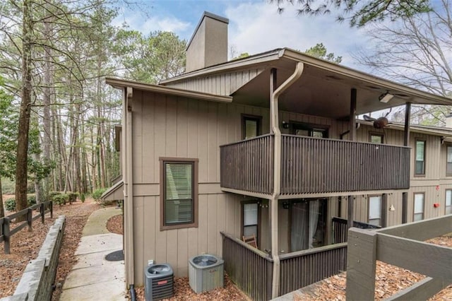 view of side of property with cooling unit, a chimney, and a balcony