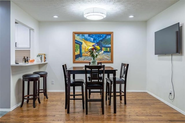 dining space with baseboards, a textured ceiling, and wood finished floors