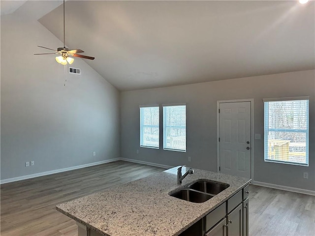 kitchen featuring light stone counters, a center island with sink, open floor plan, vaulted ceiling, and a sink