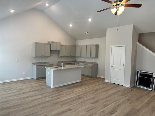 kitchen with light wood-type flooring, a sink, a kitchen island with sink, and gray cabinetry