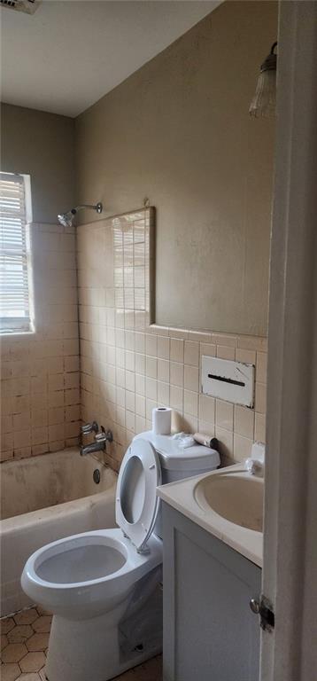 full bathroom with toilet, tile walls, vanity, tiled shower / bath combo, and tile patterned flooring