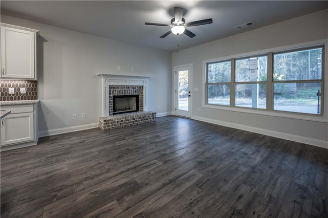 unfurnished living room featuring a brick fireplace, dark hardwood / wood-style floors, and ceiling fan