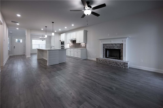 unfurnished living room with ceiling fan with notable chandelier, dark wood-type flooring, sink, and a fireplace