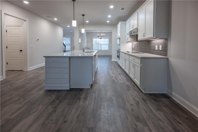 kitchen featuring white cabinetry, decorative light fixtures, a center island with sink, and backsplash