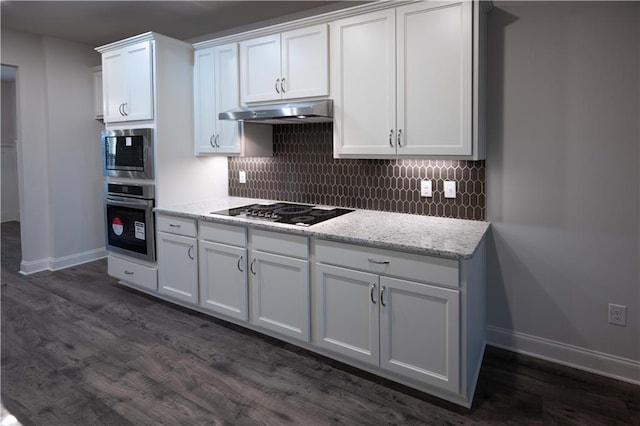 kitchen featuring appliances with stainless steel finishes, white cabinetry, dark hardwood / wood-style floors, light stone countertops, and decorative backsplash