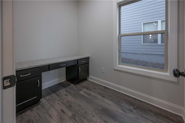 unfurnished office featuring dark hardwood / wood-style floors, built in desk, and a wealth of natural light